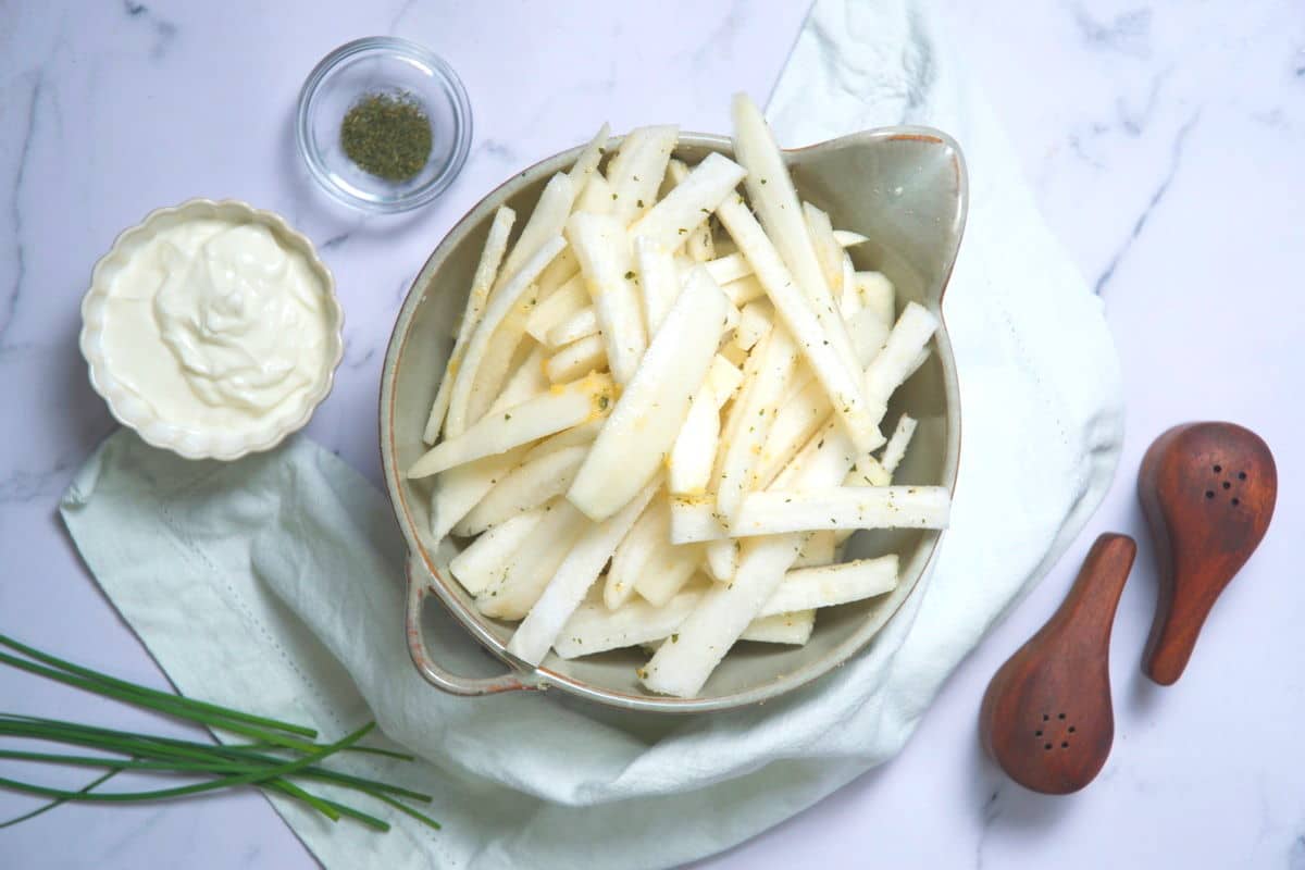 Raw turnip fries in bowl with chives, yogurt and spices on the side.