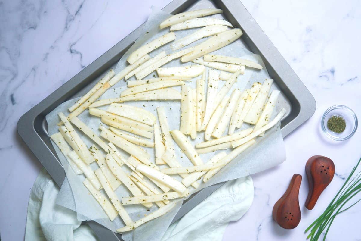 Raw turnip sticks on a large parchment-lined frying pan.