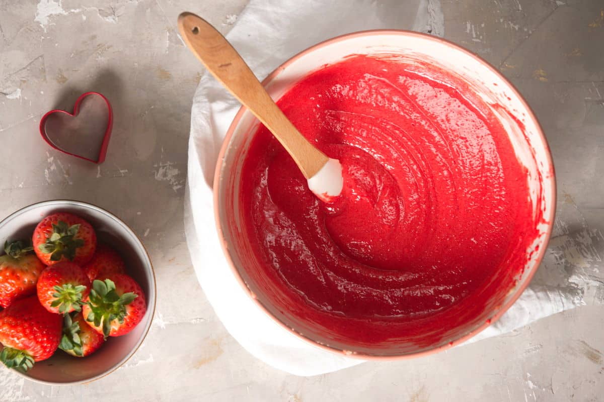 Red velvet cake batter in a bowl with a spatula and fresh strawberries on the side.