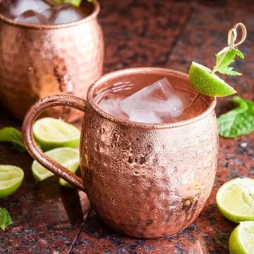 Virgin Moscow Mule in copper mugs, surrounded by sliced limes on brown-black background.