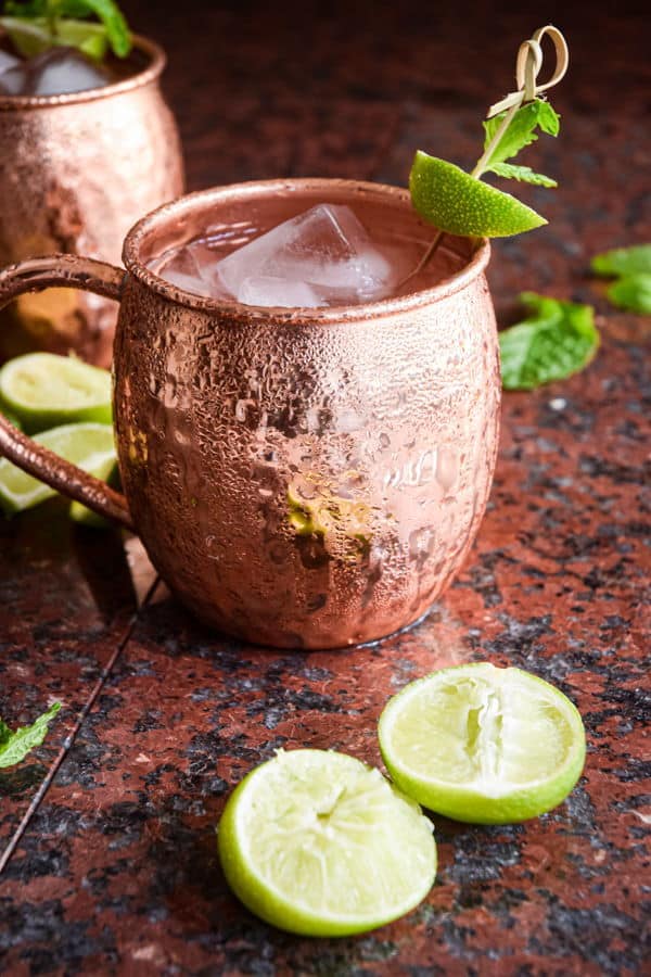 Virgin Moscow Mule in copper mugs, surrounded by sliced limes on brown-black background.