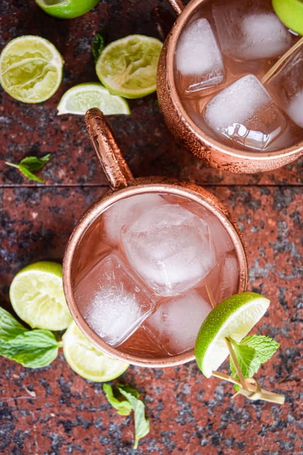 Virgin Moscow Mule in copper mugs, surrounded by sliced limes on brown-black background.