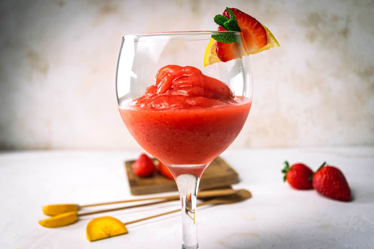 Front view of a virgin strawberry daiquiri in a glass with a strawberry, mint and lemon garnish.