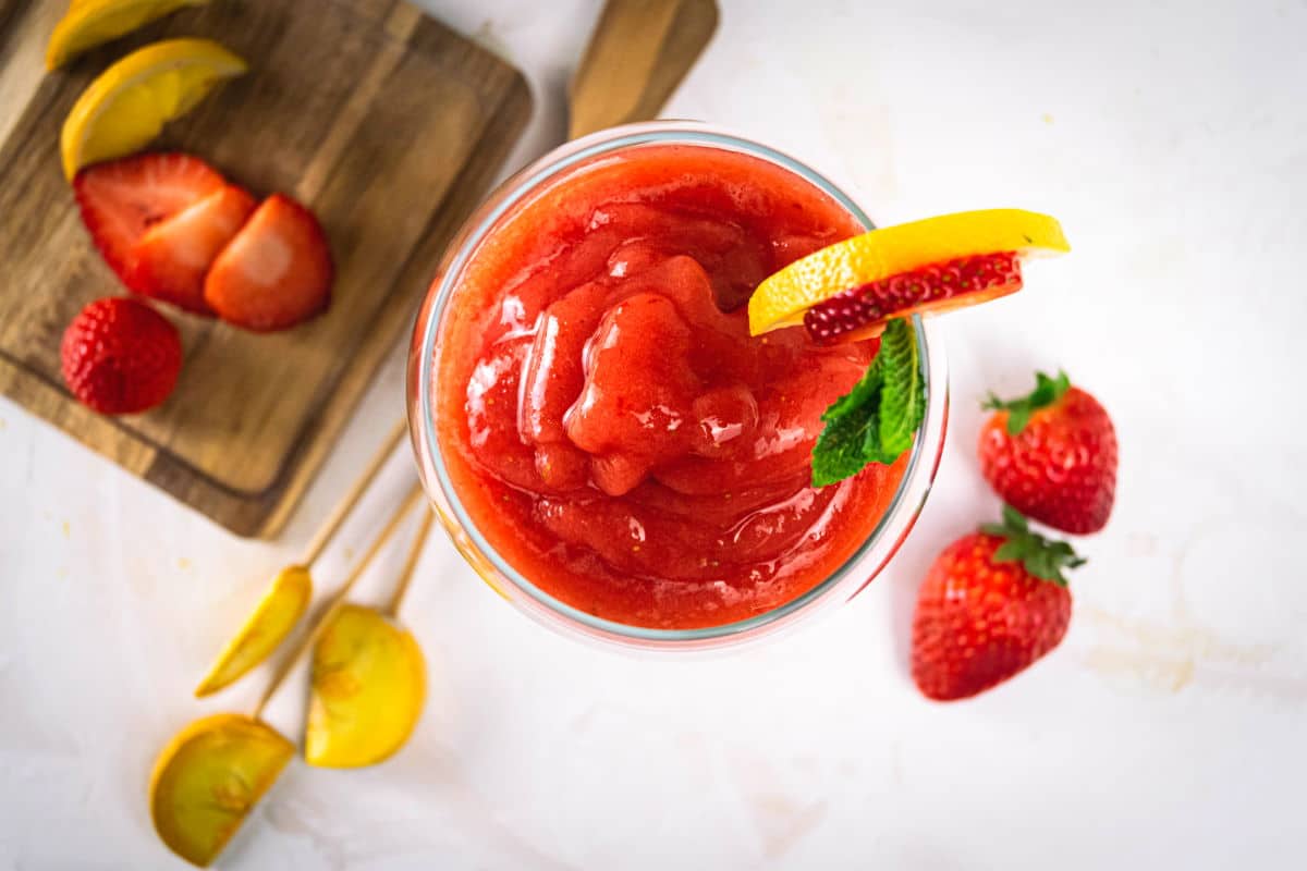 Top view of a virgin strawberry daiquiri in a glass with a strawberry, mint and lemon garnish on light background.