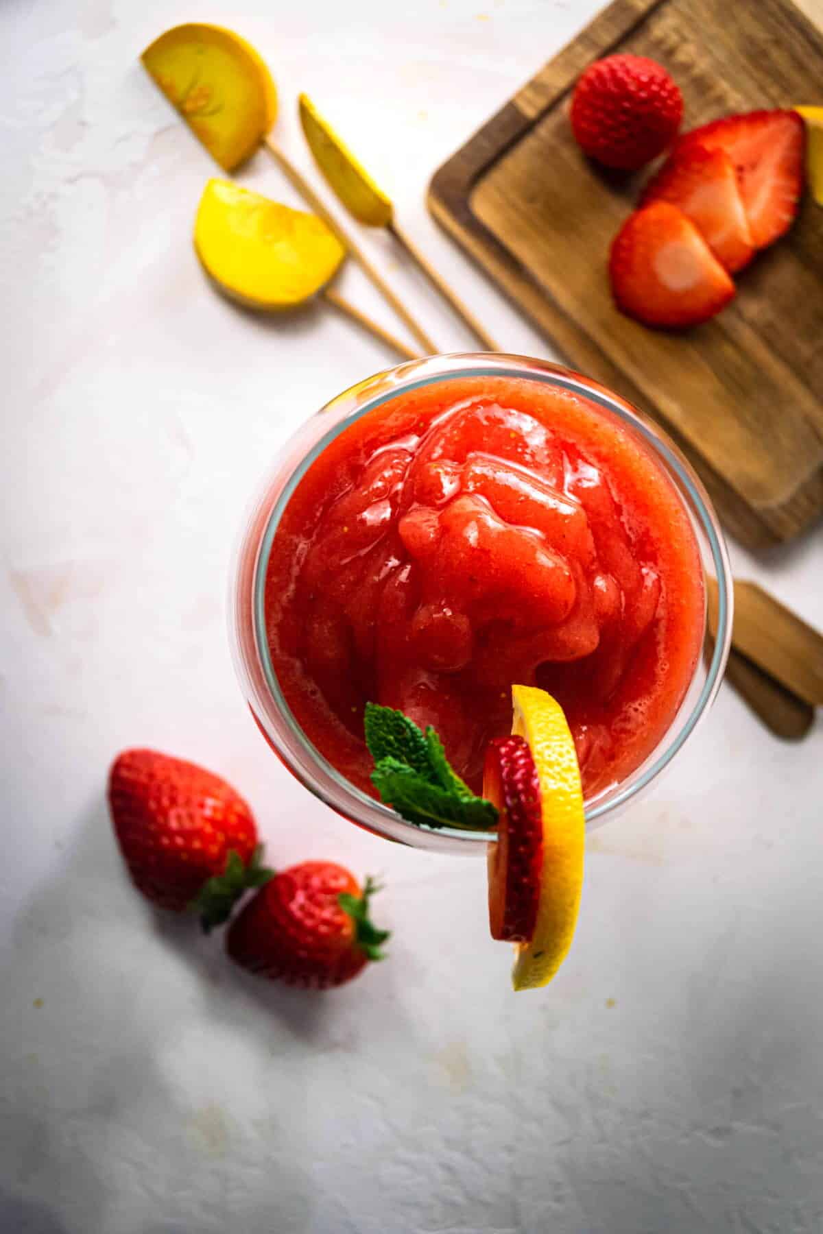 Top view of a virgin strawberry daiquiri in a glass with a strawberry, mint and lemon garnish.