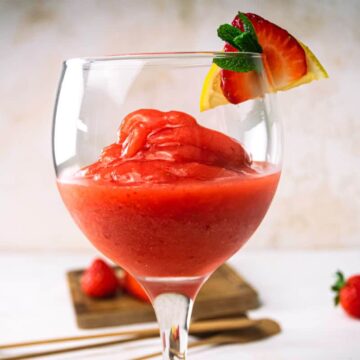 Virgin strawberry daiquiri in a glass with a strawberry, mint and lemon garnish.