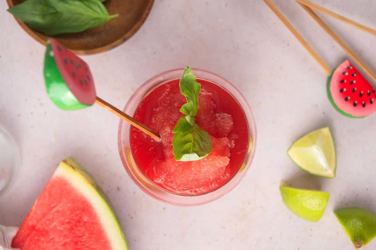 Top view of watermelon basil cocktail in wine glass with a watermelon stir stick and lime wedges on the side.