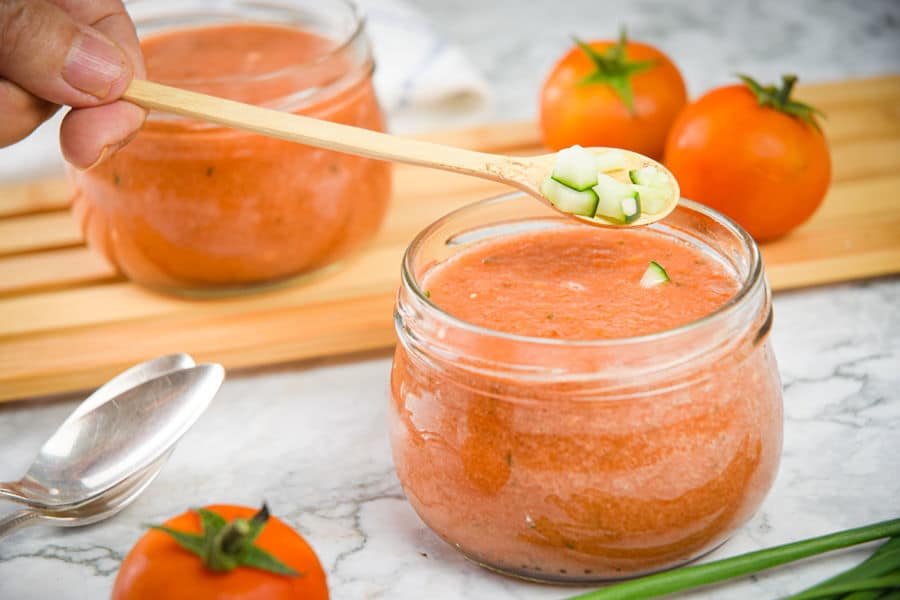 Watermelon gazpacho in a jar, diced cucumber on top, tomatoes in the background.