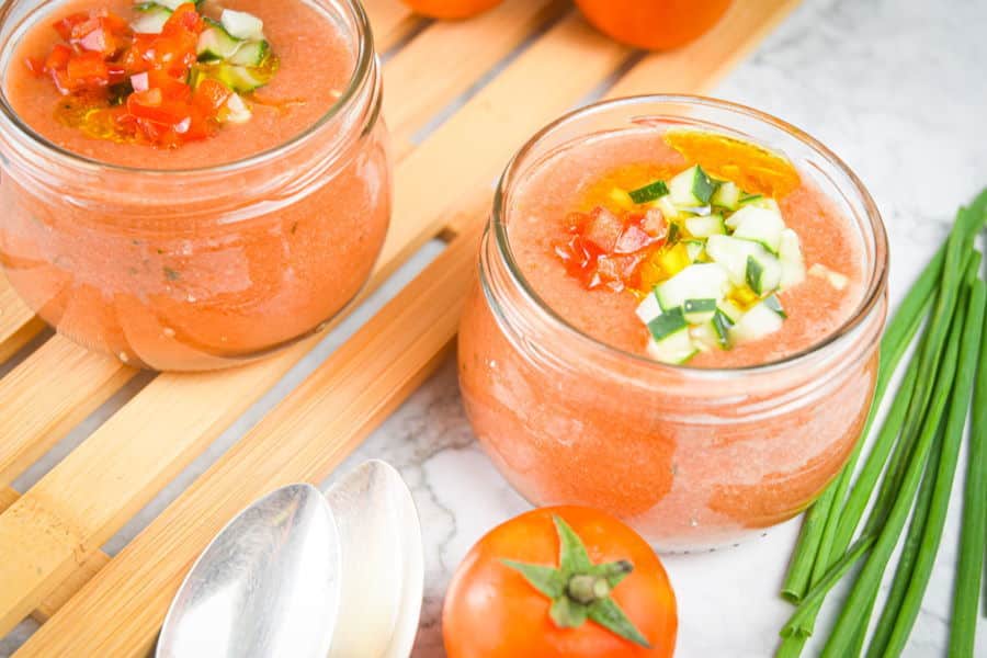 Watermelon gazpacho in a jar, diced veggies on top, tomatoes in the background.