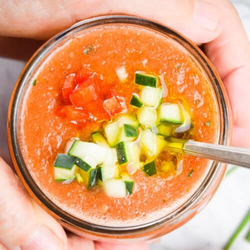 Watermelon gazpacho in a glass jar with a spoon, held in hands.