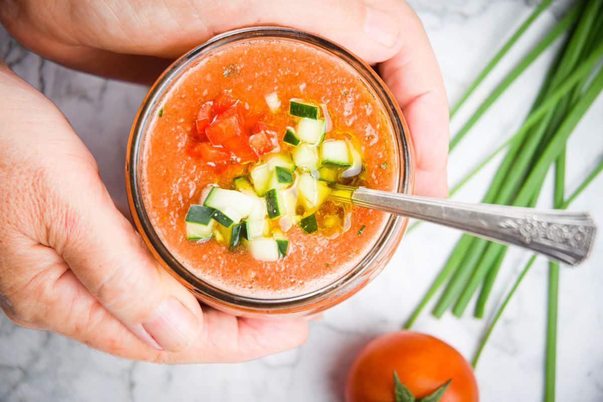 Watermelon gazpacho in a glass jar with a spoon, held in hands.