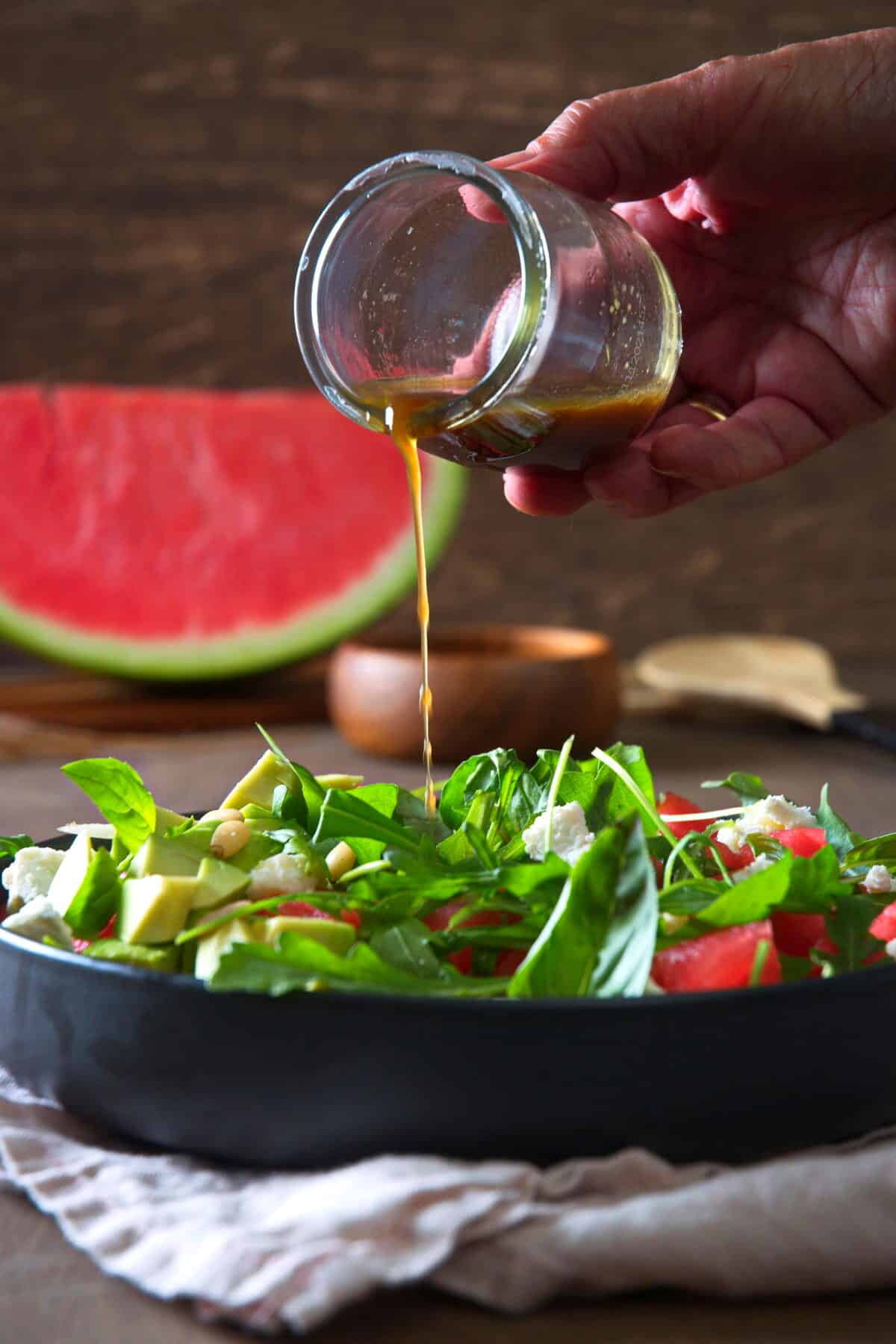 Watermelon salad in a black salad bowl with vinaigrette drizzling over, front view.