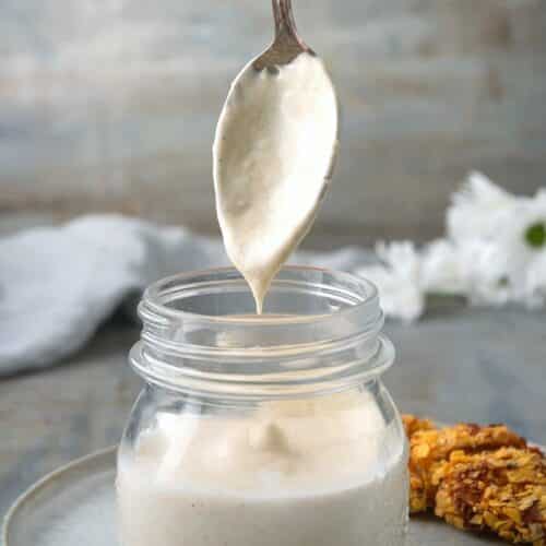 White BBQ sauce in a small jar with a spoon.