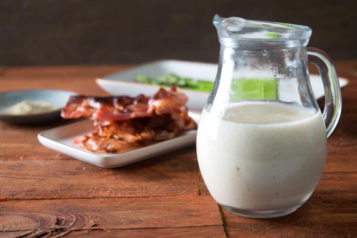 White gravy in a jar with bacon and asparagus in the background.