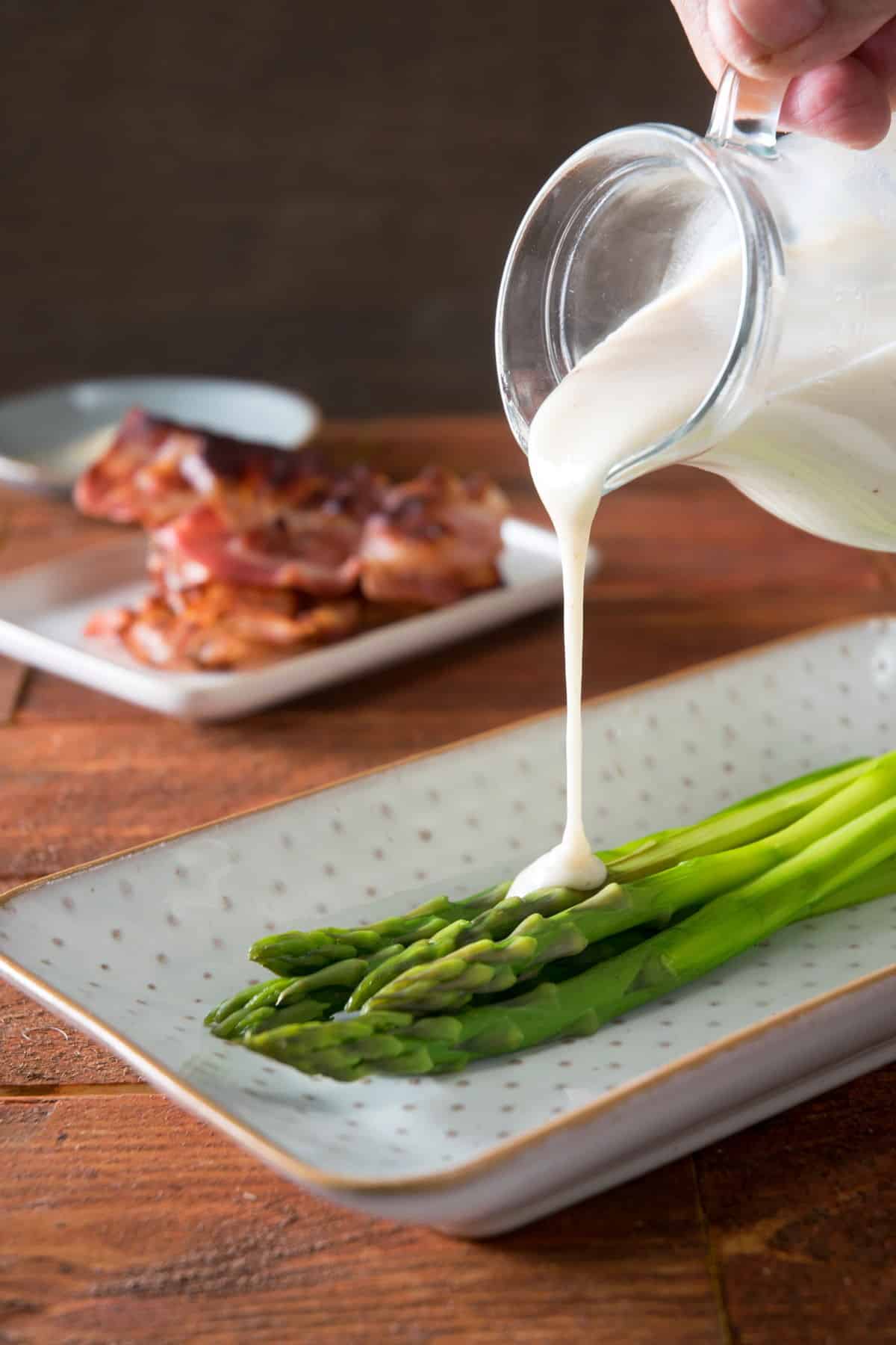 White gravy in a jar, drizzling over cooked asparagus.