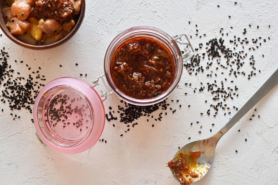 XO sauce in a jar on white background with black sesame seeds scattered around.