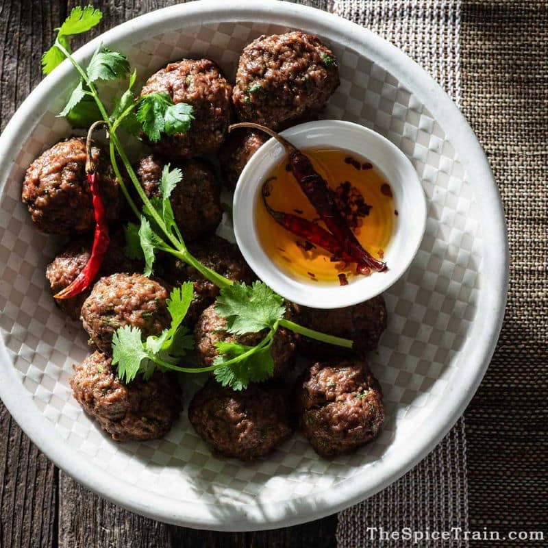 Beef Meatballs on white plate with cilantro on top and an oil dip.
