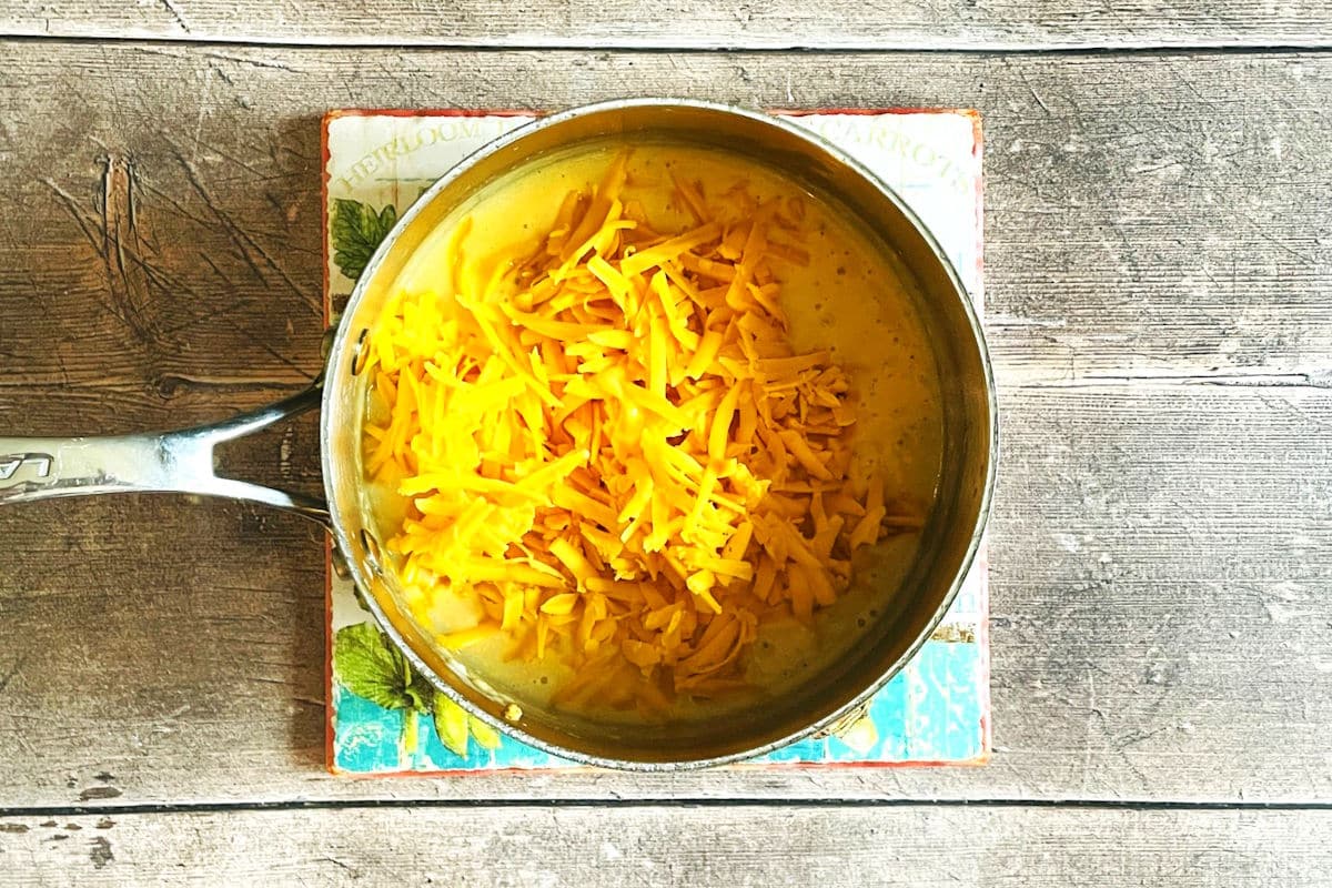 Beer cheese dip mixture in saucepan with shredded cheddar.