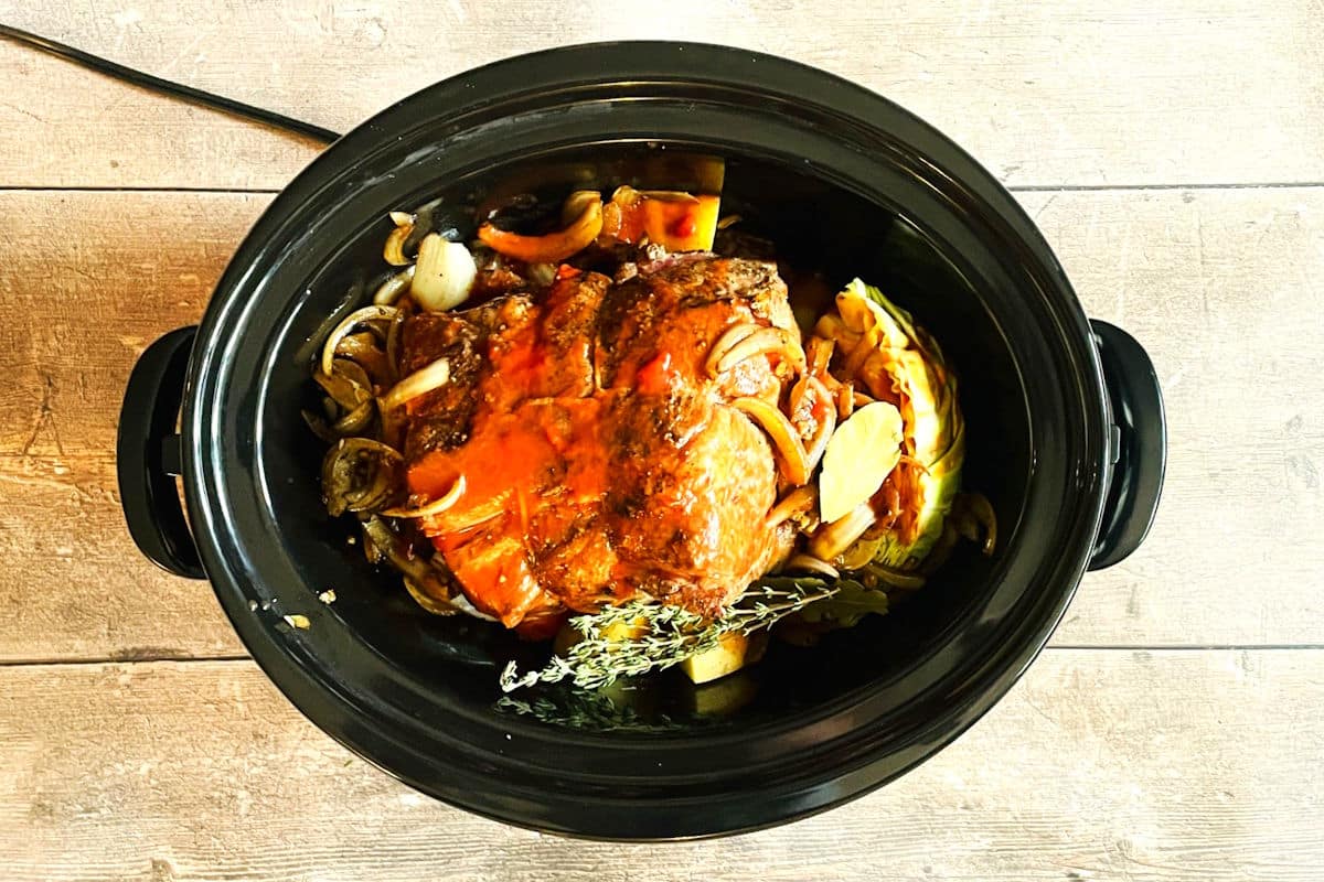 Bison roast, vegetables, herbs and sauce in slow cooker.