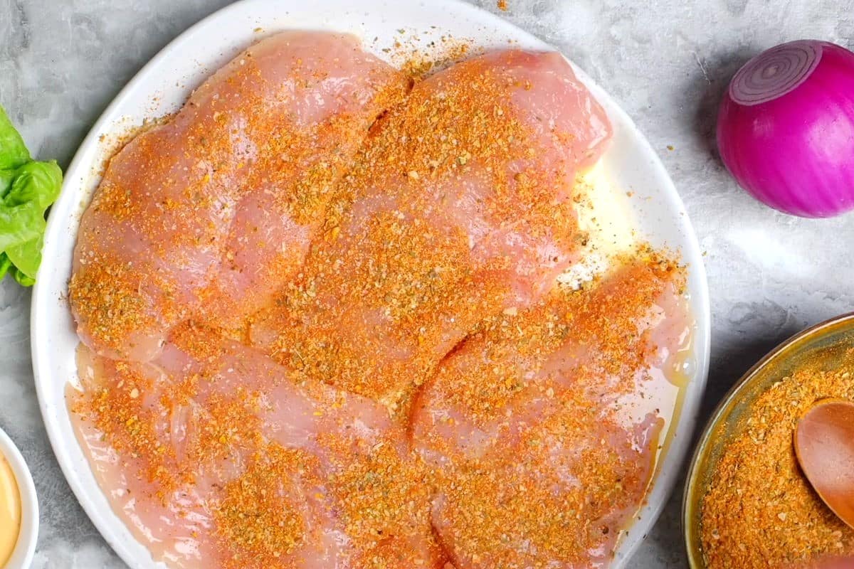 Raw chicken breasts on a plate, covered in blackening spices.