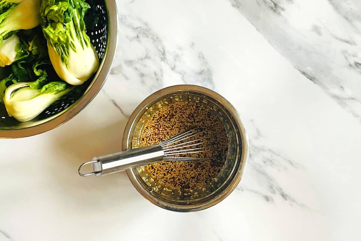 Bok choy stir fry sauce in bowl with whisk and baby bok choy on the side.