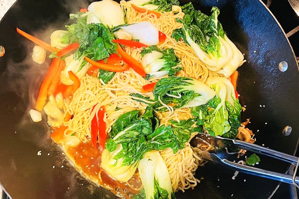 Bok choy noodle stir fry in wok with stir fry sauce.