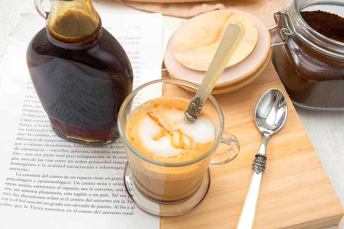 Hot caramel coffee in a mug with a glass bottle of caramel syrup on the side.