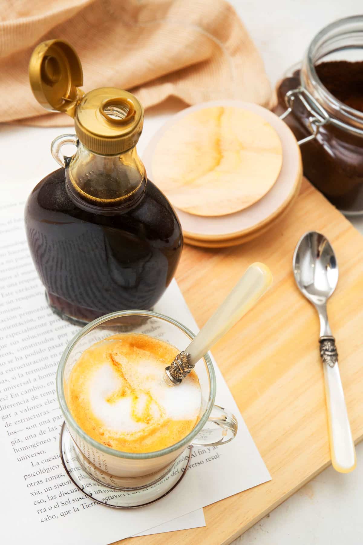 Open bottle of caramel syrup by a mug of hot coffee.