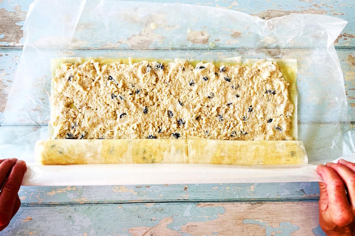 Raw cheese strudel getting rolled up by woman.