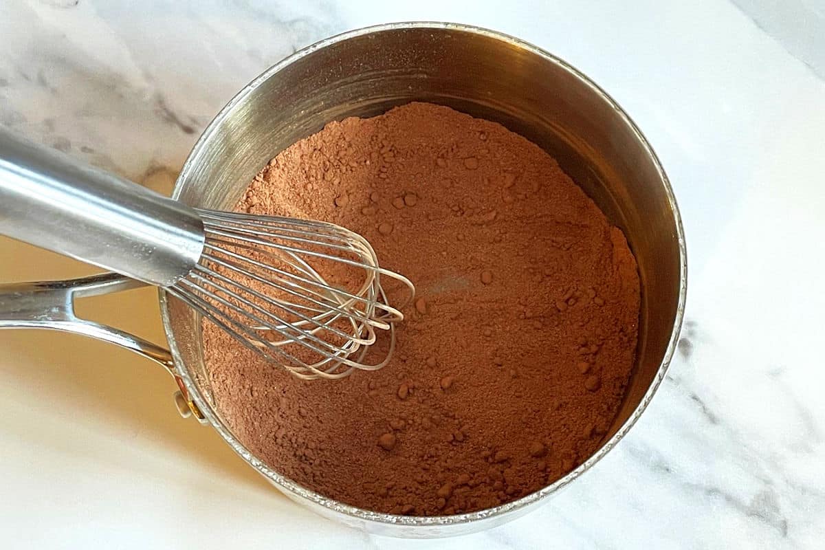 Chocolate gravy dry ingredients in saucepan with whisk.
