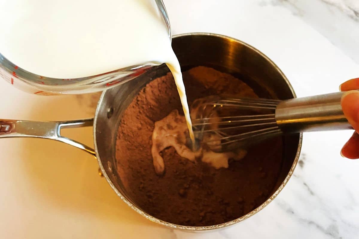 Milk getting whisked into cocoa powder mixture in saucepan.