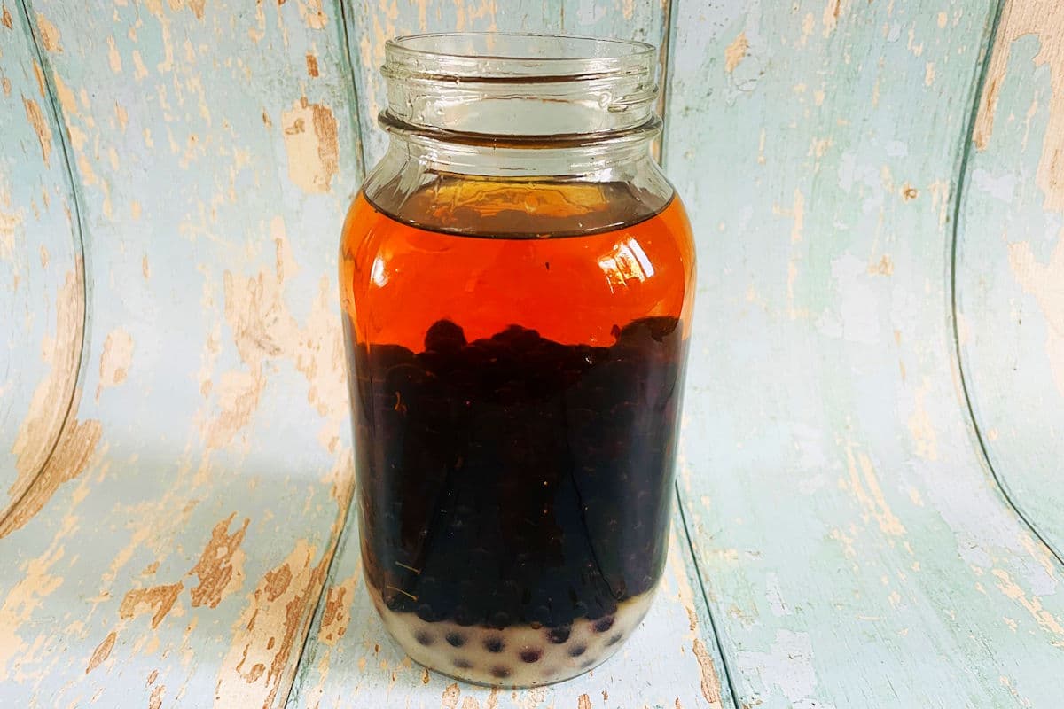 Chokecherries, sugar and spirits in jar on wooden background.