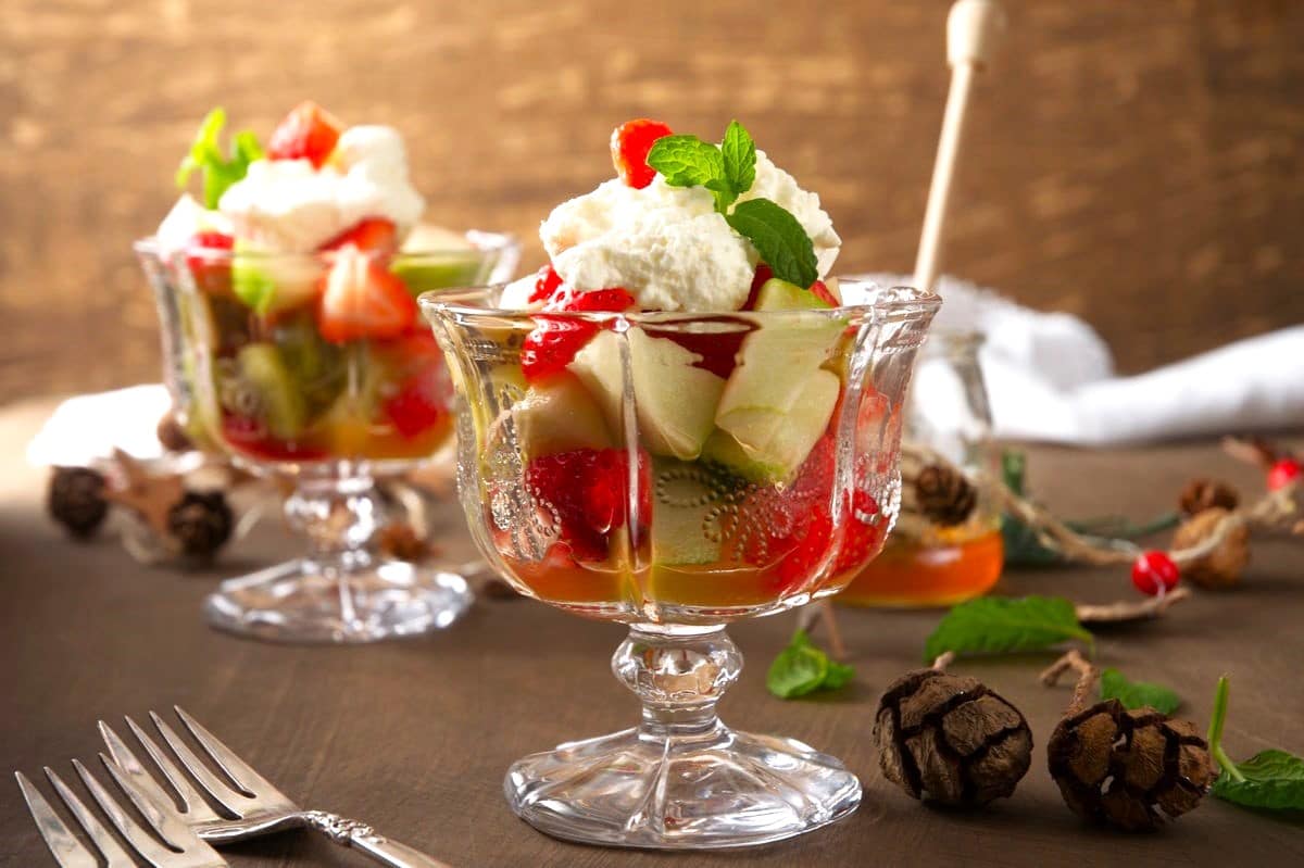 Fruit salad with whipped cream and mint in dessert glasses.