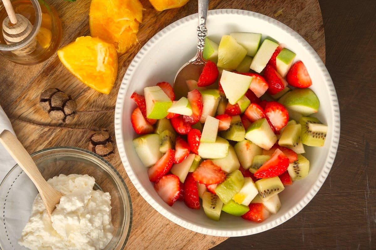 Fruit salad in white bowl with a spoon.