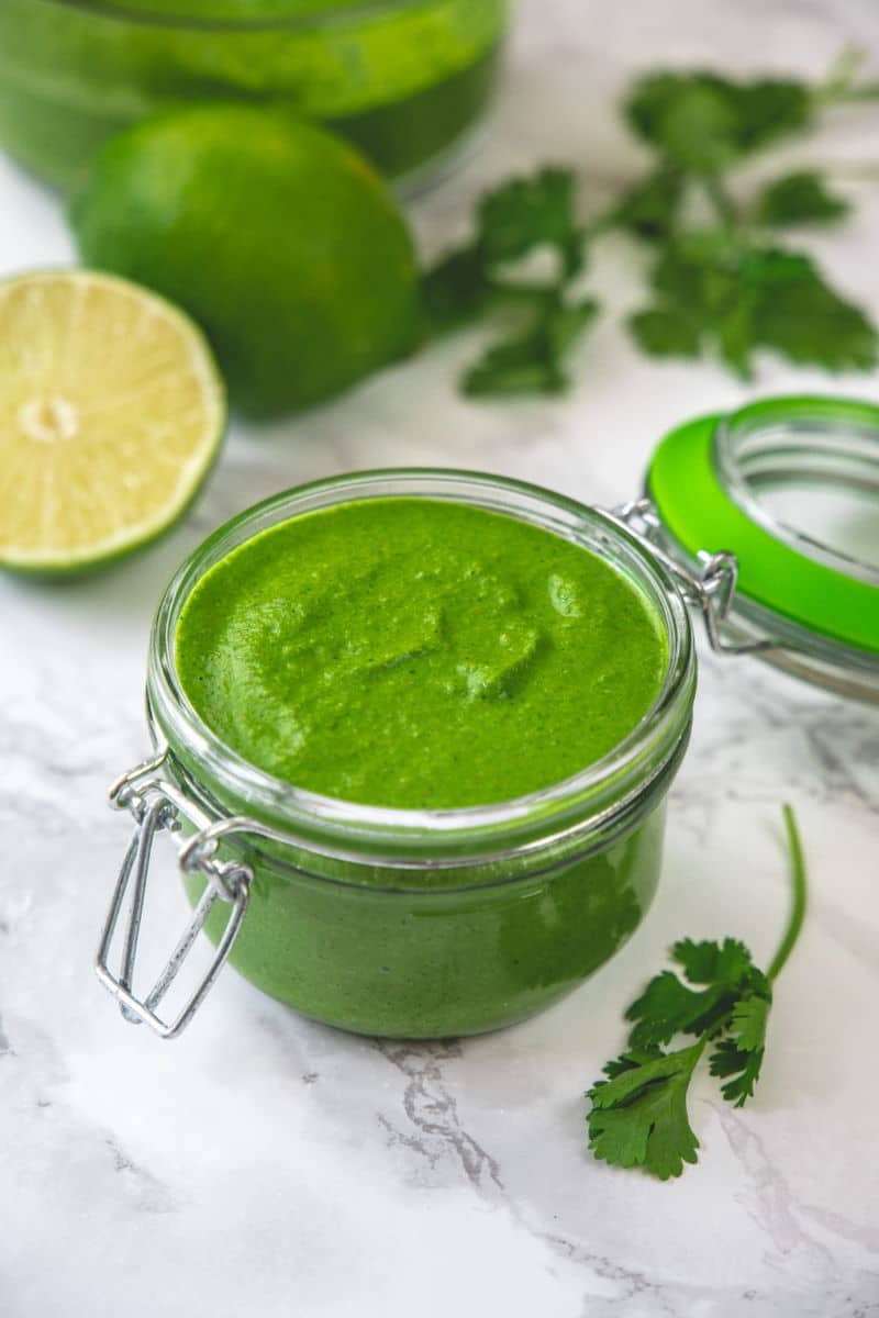 Cilantro chutney in a jar with cilantro leaves on the side.