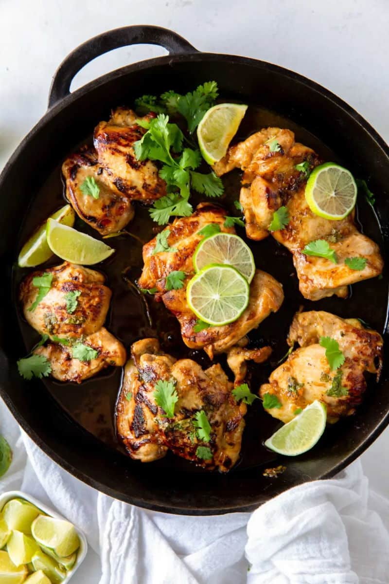 Chicken thighs in cast iron pan with lime slices and cilantro leaves.