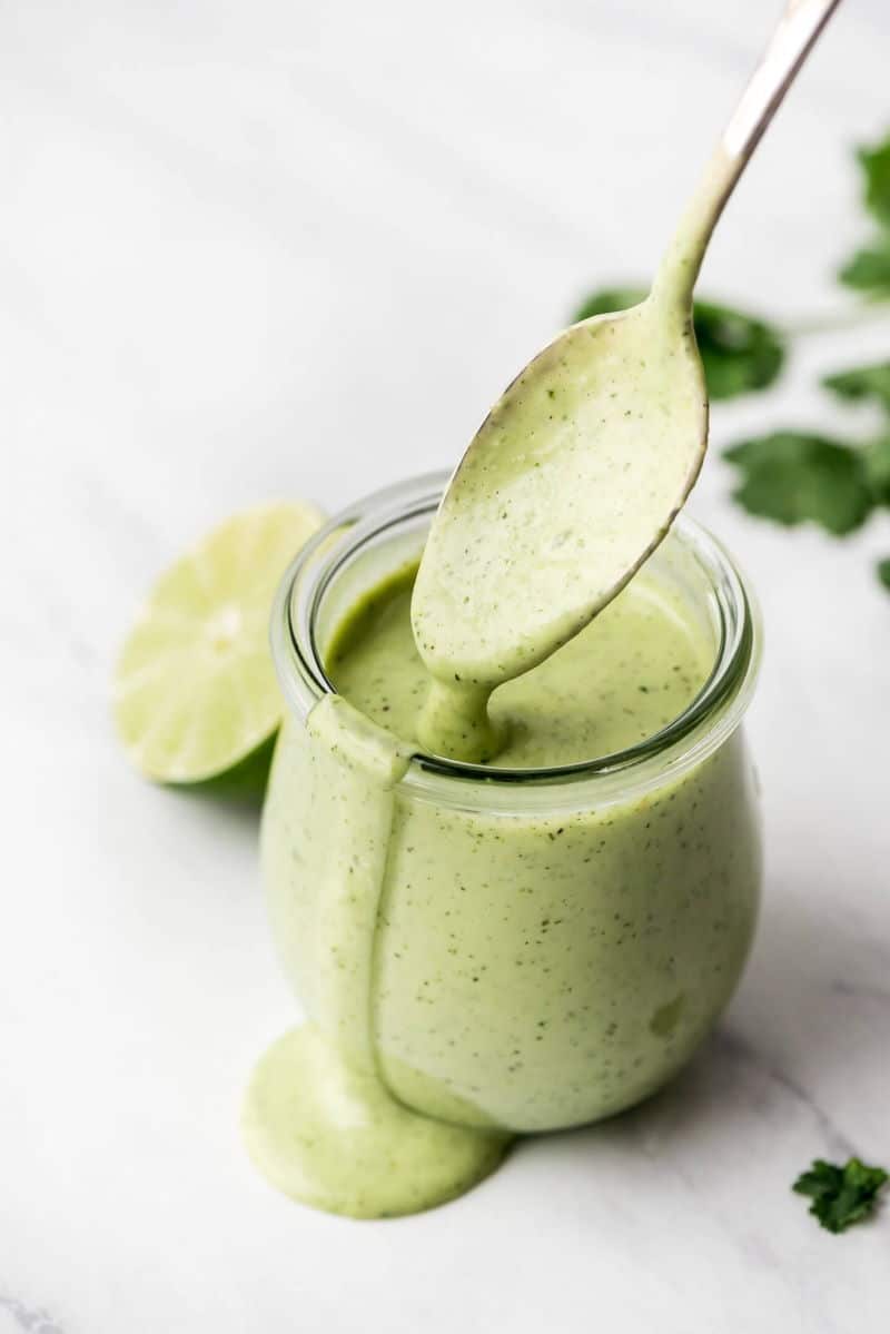 Creamy cilantro dressing in a small glass jar with spoon, marble background.