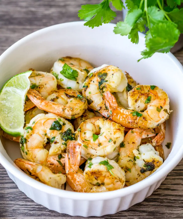 Cilantro shrimp with lime wedge in a white ramekin.