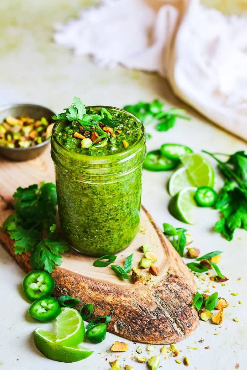 Cilantro pesto in small jar on wooden board.