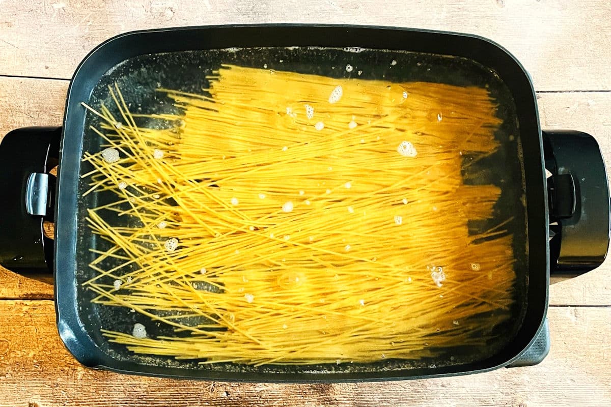 Spaghetti noodles cooking in electric skillet.