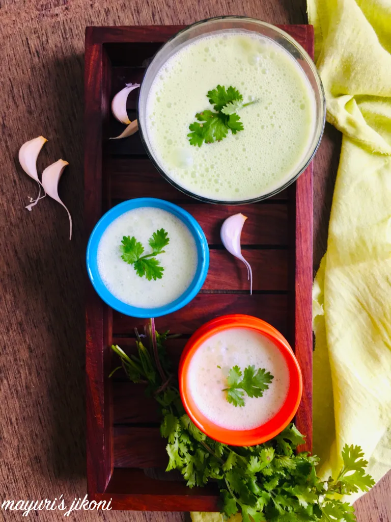 Chaas in cups on wooden board, garlic cloves and cilantro bunch on the side.