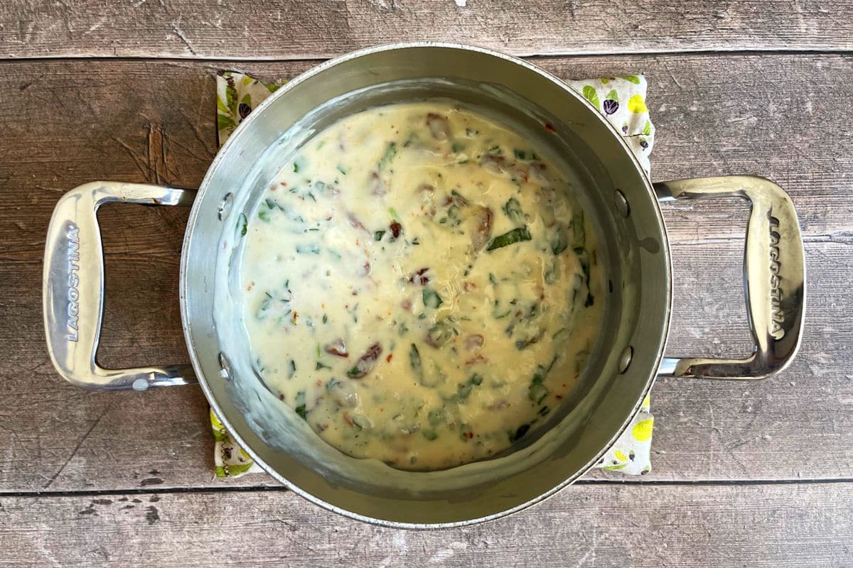 Cheese sauce with herbs in saucepan.