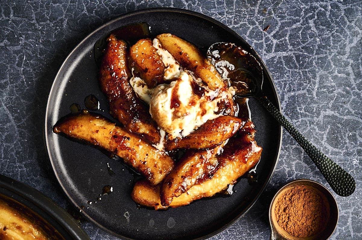 Bananas Foster with ice cream and spoon on black plate.