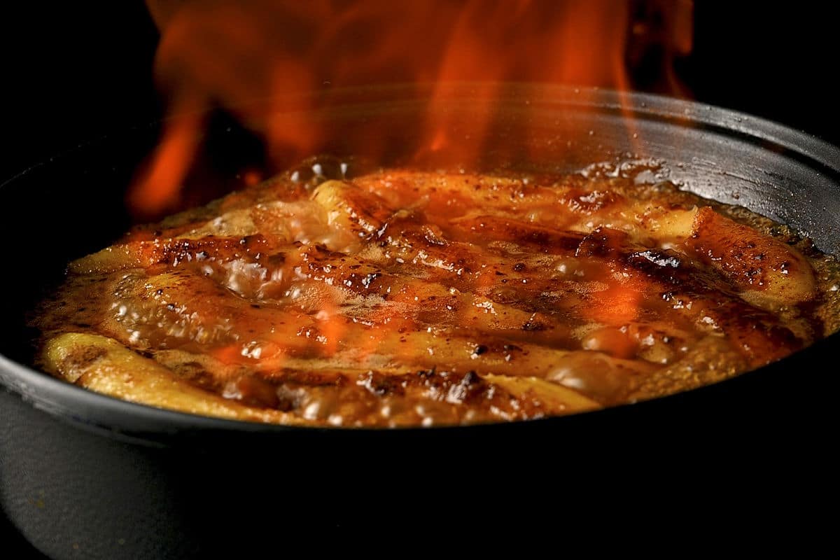 Bananas getting flambeed with fire in skillet.