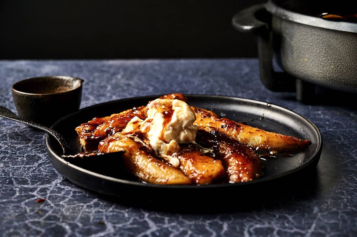 Bananas Foster (flambeed bananas) on black plate with spoon and ice cream.