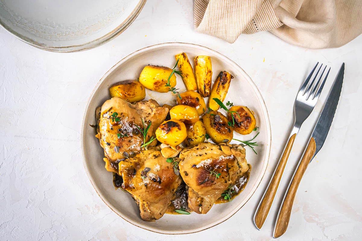 Greek lemon chicken thighs and baby potatoes on plate with fork and knife.