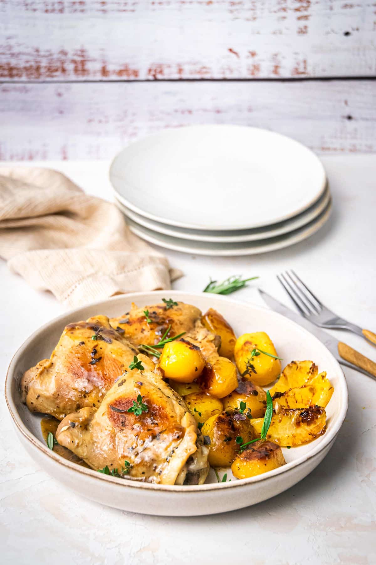 Greek lemon chicken thighs and baby potatoes on plate, white background.