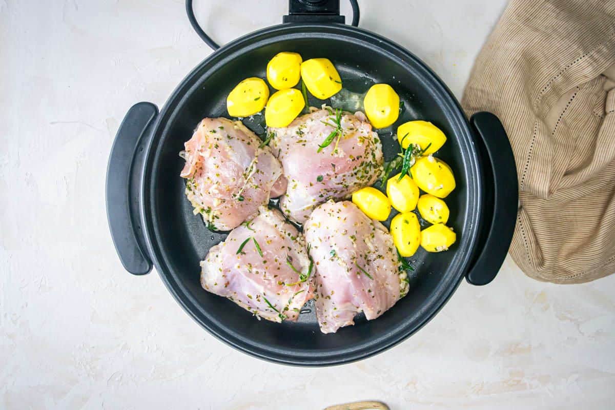 Raw chicken thighs and potatoes in electric skillet.