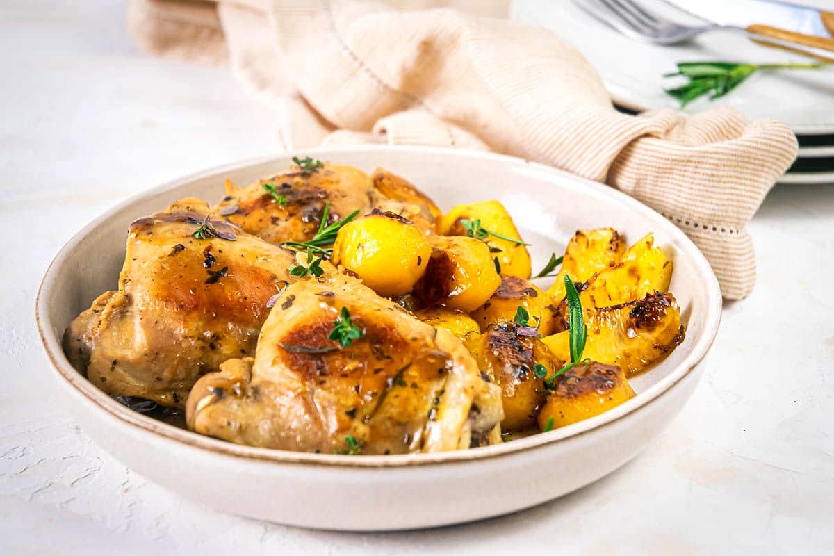Greek lemon chicken thighs, potatoes and herbs in white plate.
