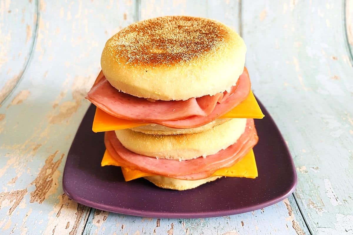 English muffin sandwiches stacked on plate on wooden background.